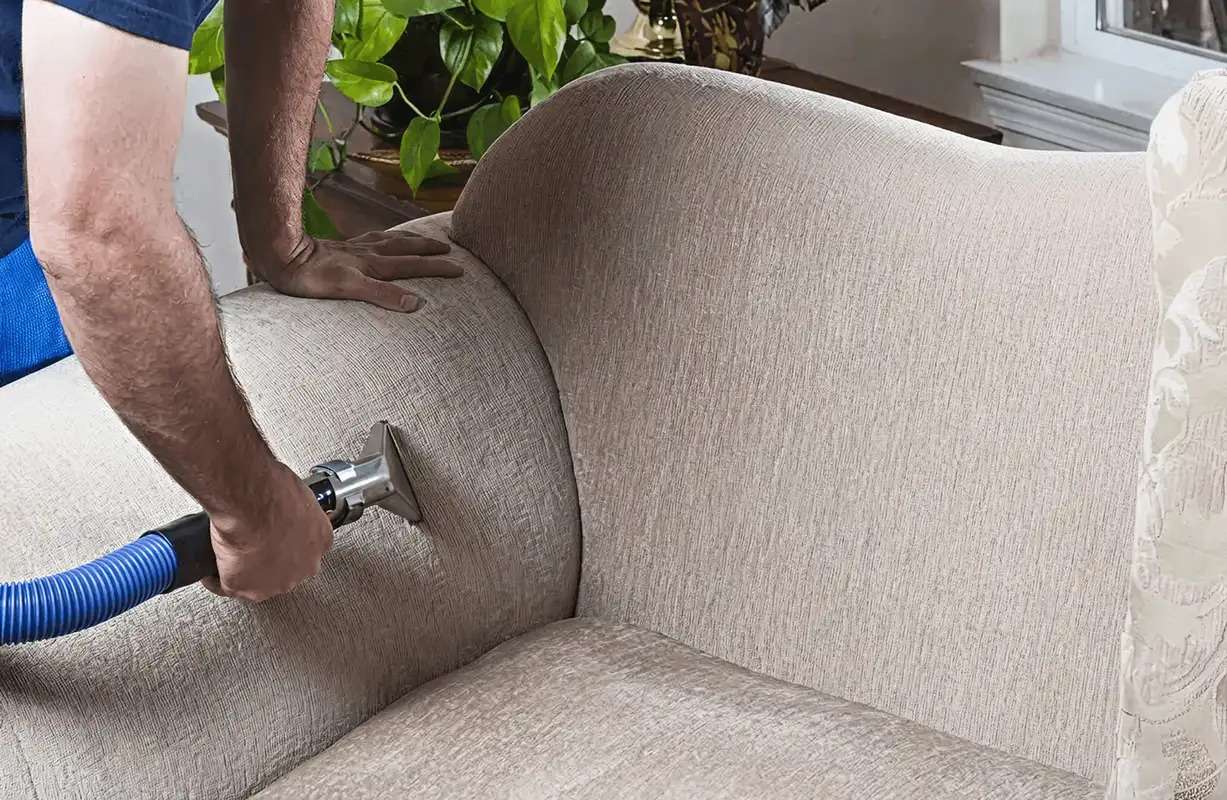 Professional upholstery cleaner deep-cleaning a fabric sofa with a handheld extraction tool and hose, Lakeland, FL.